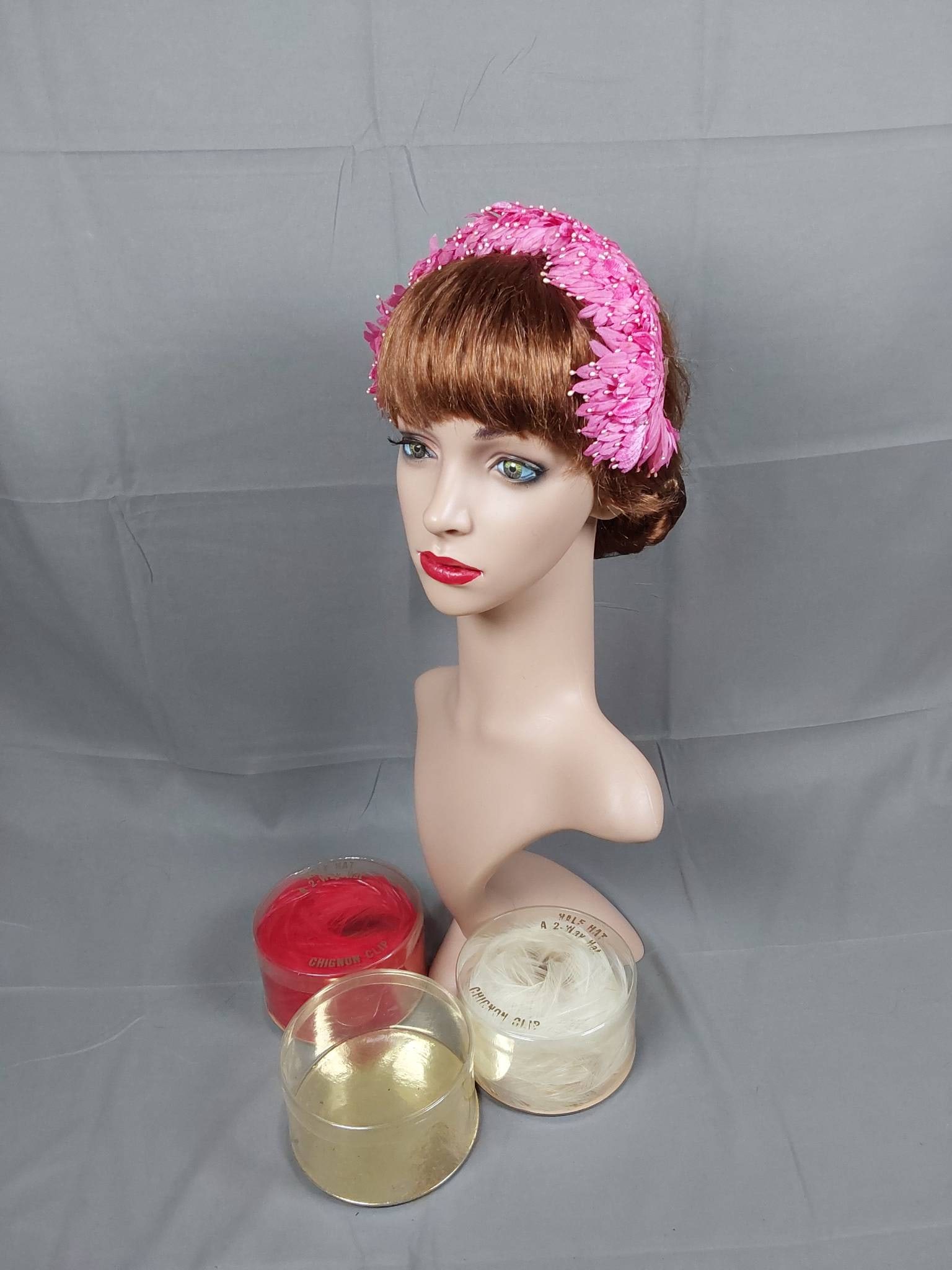 3 Vintage Half Hats in Boxes: A group of 3 vintage 1950s half hats/chignon clips in a variety of styles. Included is a layered pink silk and pink velvet floral half hat featuring pink pearl-like accents. It is in good to fair cond