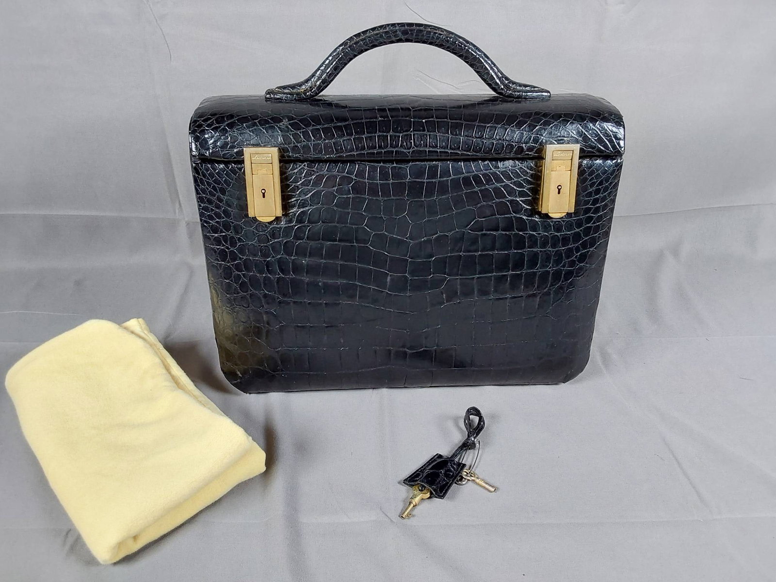 Vintage Lederer Ladies Cosmetic Travel Case: Vintage Lederer ladies cosmetic travel case featuring a black crocodile body with a sturdy top handle, two lockable brass buckles, and two included keys. The case is equipped with four brass feet for 