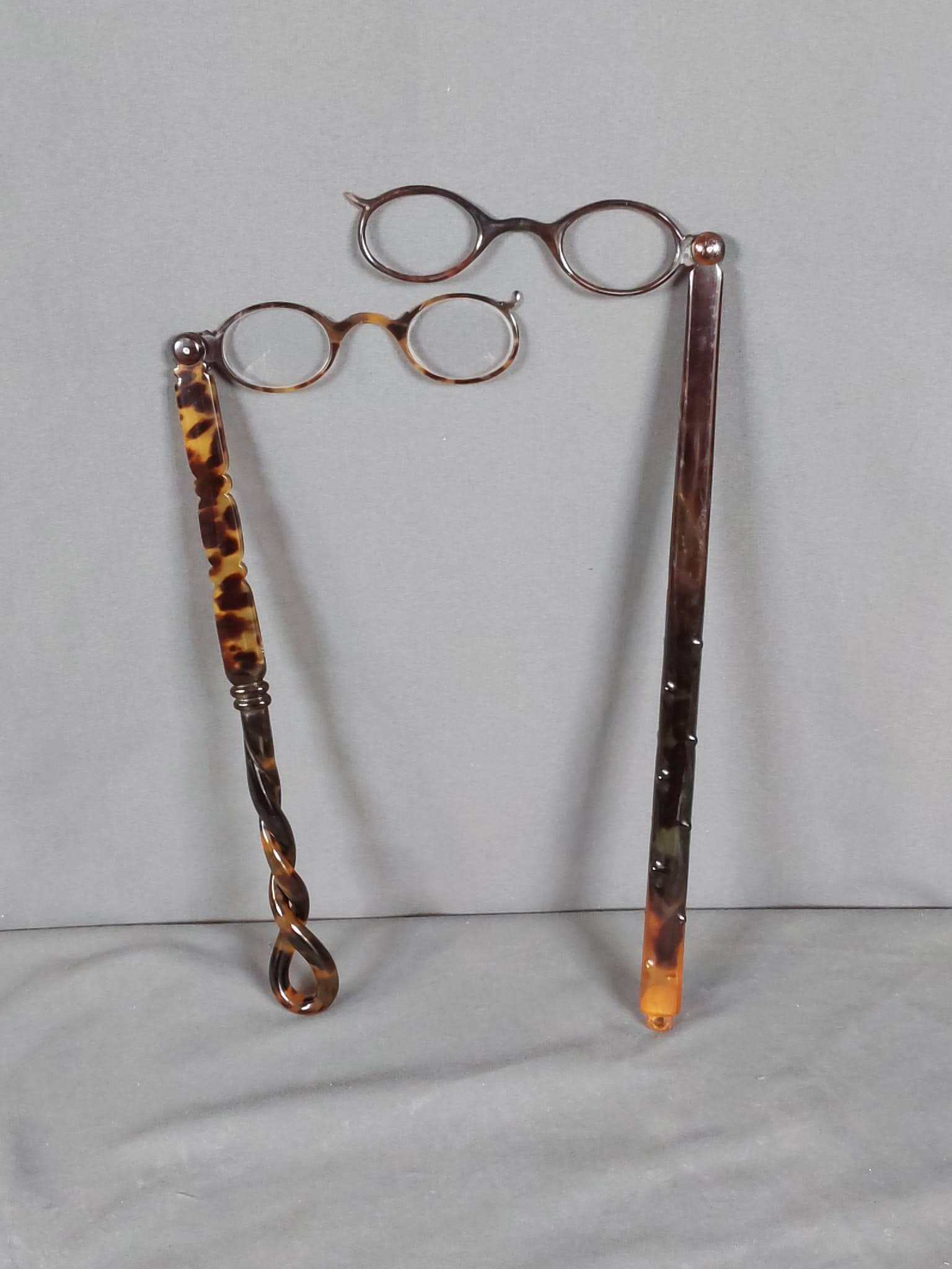 Early 20th Century Faux Tortoise Lorgnettes: Lot featuring two pairs of early 20th century faux tortoise shell lorgnettes. The first pair measures 10 3/4 inches in length and is crafted from early plastic with a faux tortoise shell design. It fe