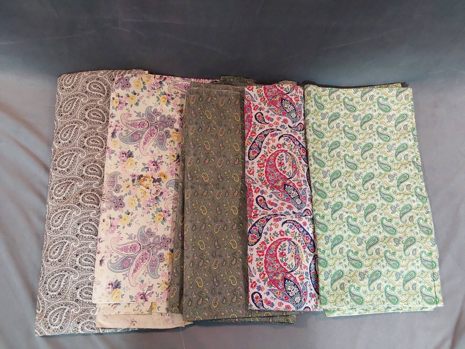 Vintage Cotton Fabric - Paisleys: A lot of five pieces of vintage cotton fabric featuring colorful paisley designs. The fabric lot weighs 3.1 lbs and measures 8 yards or less in total. Designs include shades of white, green, purple, y