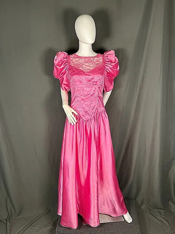 Vintage c1980 Formal Pink Gown: Vintage c1980 Formal Pink Gown. The lot includes a size 13/14 vintage c1980 formal gown featuring a shell made of pink acetate satin. As well as classic 80’s details such as puffed short sleeves, pi
