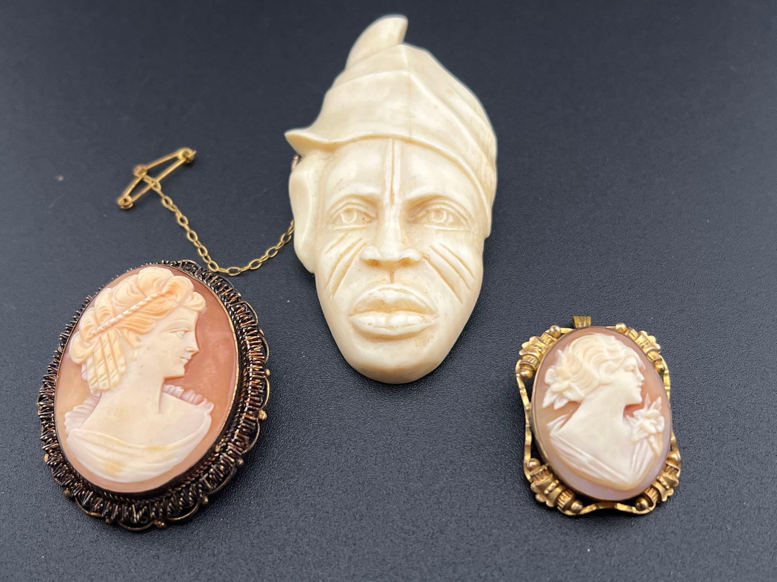 Cameos and Carved Faces: A shell cameo set in a gold filled frame 1.25” high, a shell cameo set in spun silver with a gold wash 1.5” high and a carved bone face brooch 3” high.If you have any doubt, please a