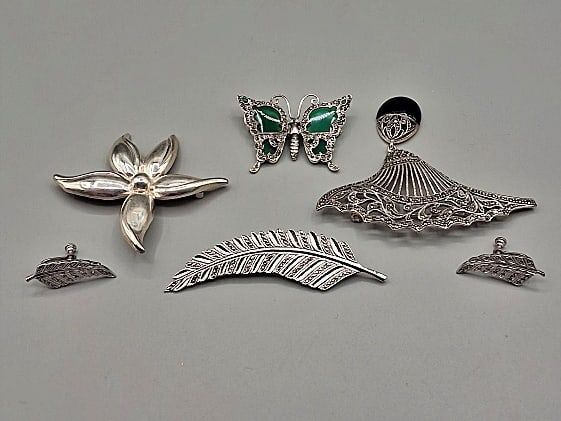 4 Sterling Brooches: Four brooches to include: A butterfly brooch with marcasites and green stone (One green stone is chipped on the back); a floral brooch with five petals; a filigree brooch with marcasites and onyx (3 1