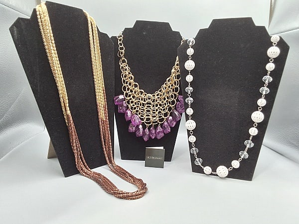 3 R.J. Graziano Necklaces: A large gold tone necklace with linked hoops in a netted style fashion with 14 purple gem-style drops (Approx. 11in Long from clasp to bottom of drop), an adjustable silver tone necklace with linked c