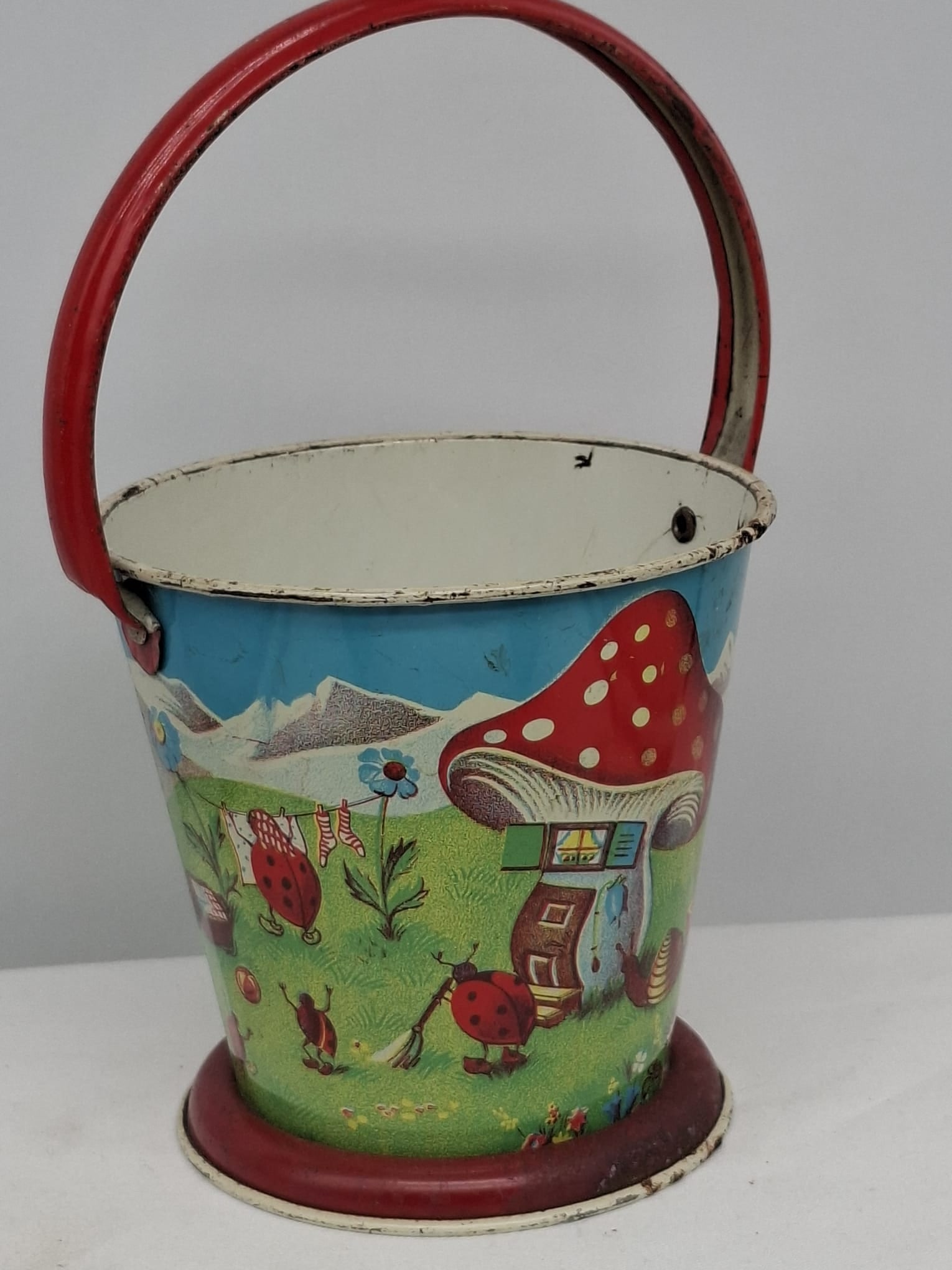 Early 20th Century Lithographed Tin Sand Pail – From Extensive European Collection: A charming and increasingly scarce early 20th century lithographed tin sand pail, exemplifying the colorful and imaginative design of classic seaside toys. This piece features vibrant period lithograp