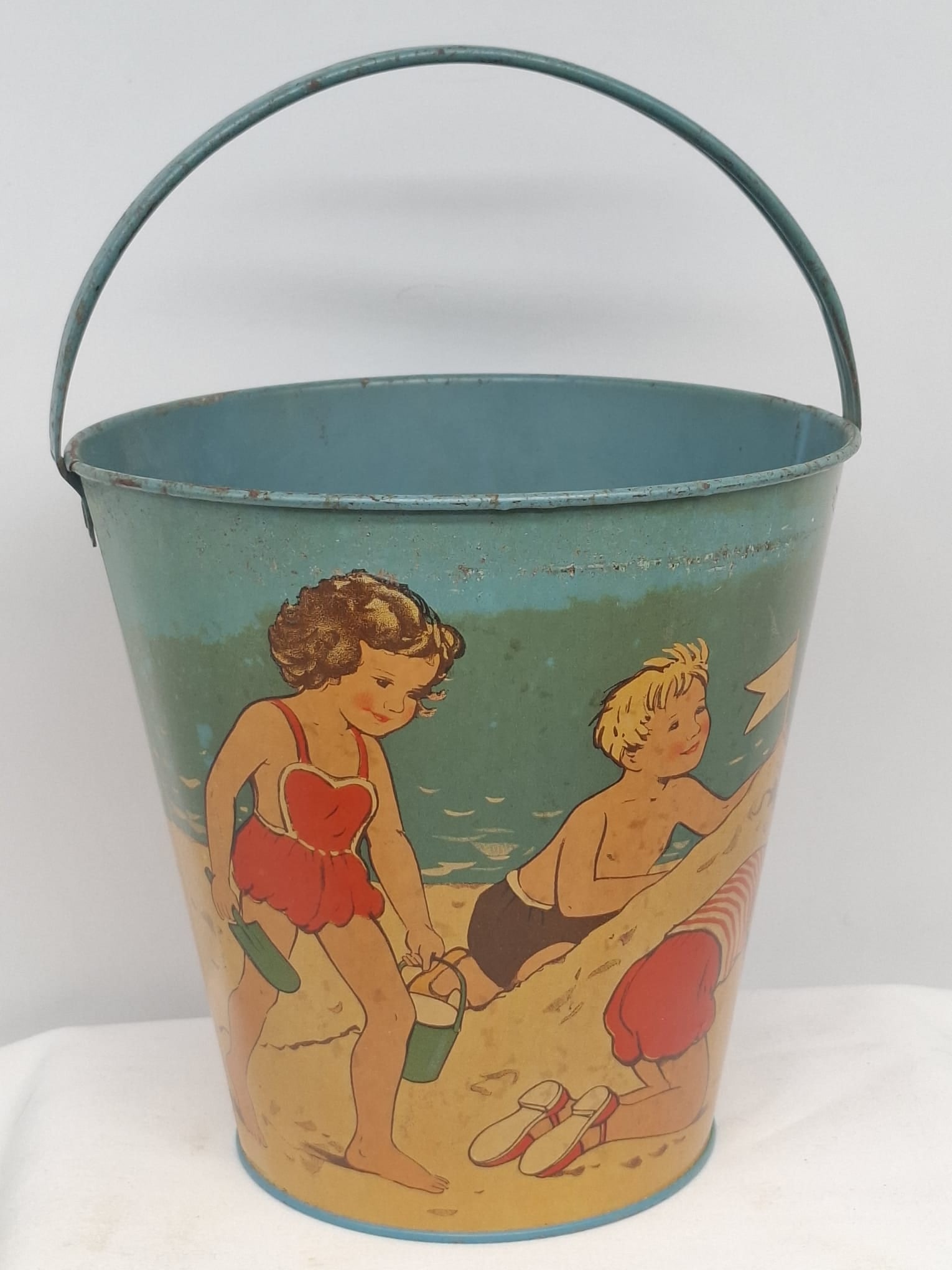 Early 20th Century Lithographed Tin Sand Pail – From Extensive European Collection: A charming and increasingly scarce early 20th century lithographed tin sand pail, exemplifying the colorful and imaginative design of classic seaside toys. This piece features vibrant period lithograp