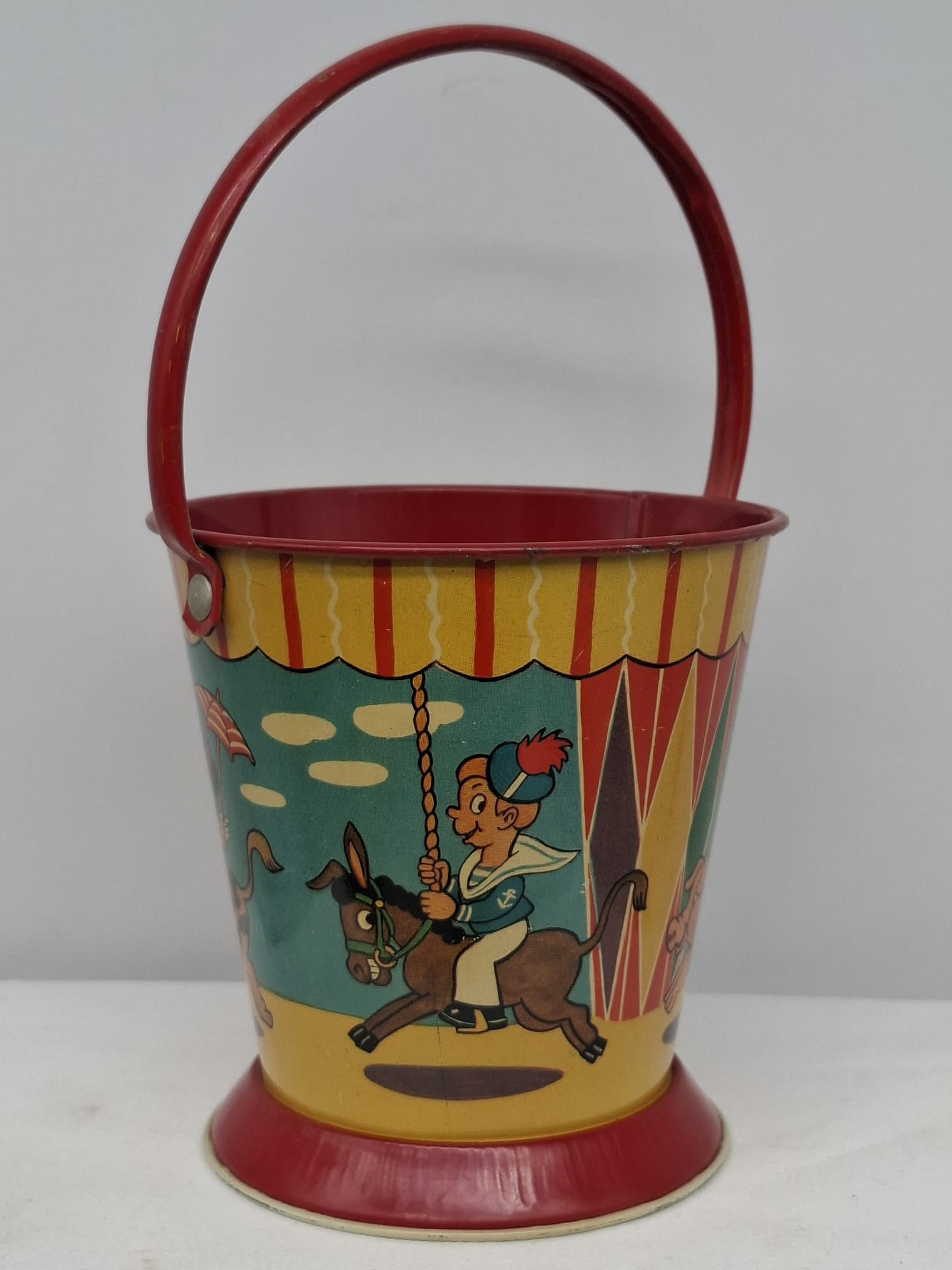 Early 20th Century Lithographed Tin Sand Pail – From Extensive European Collection: A charming and increasingly scarce early 20th century lithographed tin sand pail, exemplifying the colorful and imaginative design of classic seaside toys. This piece features vibrant period lithograp