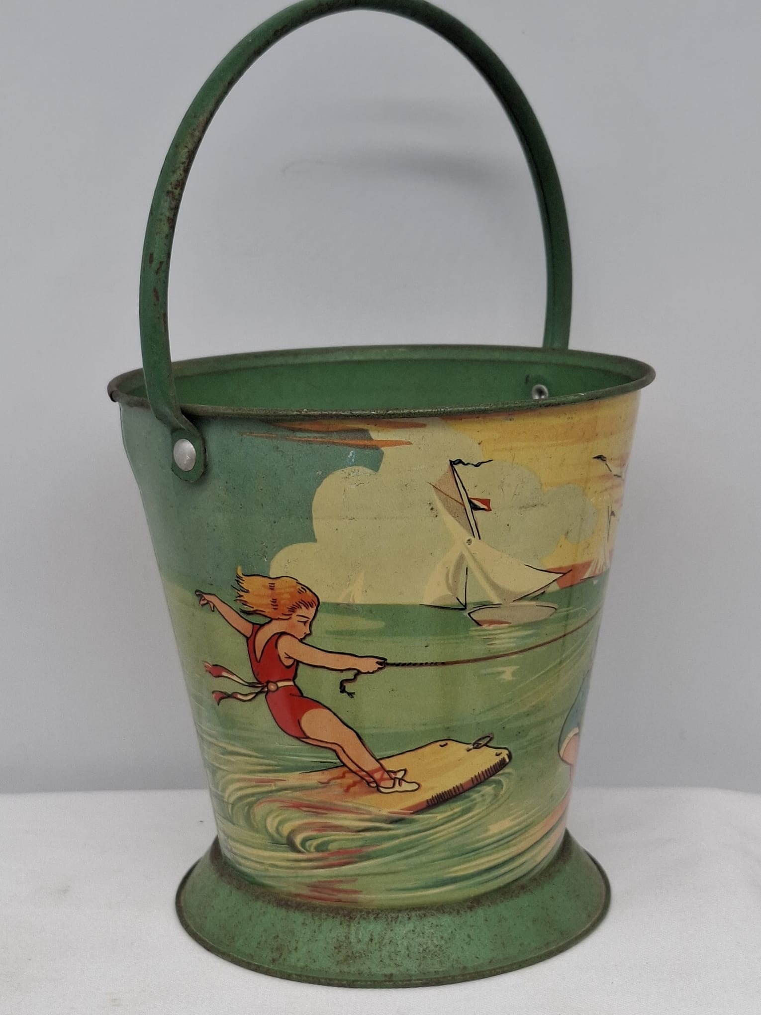 Early 20th Century Lithographed Tin Sand Pail – From Extensive European Collection: A charming and increasingly scarce early 20th century lithographed tin sand pail, exemplifying the colorful and imaginative design of classic seaside toys. This piece features vibrant period lithograp