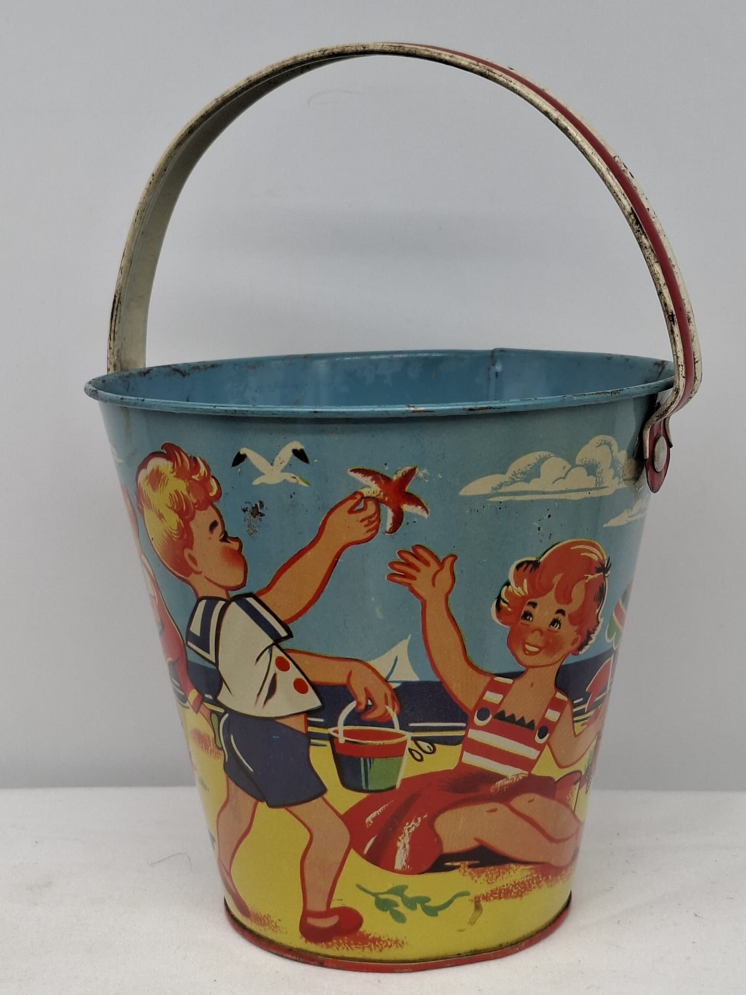 Early 20th Century Lithographed Tin Sand Pail – From Extensive European Collection: A charming and increasingly scarce early 20th century lithographed tin sand pail, exemplifying the colorful and imaginative design of classic seaside toys. This piece features vibrant period lithograp