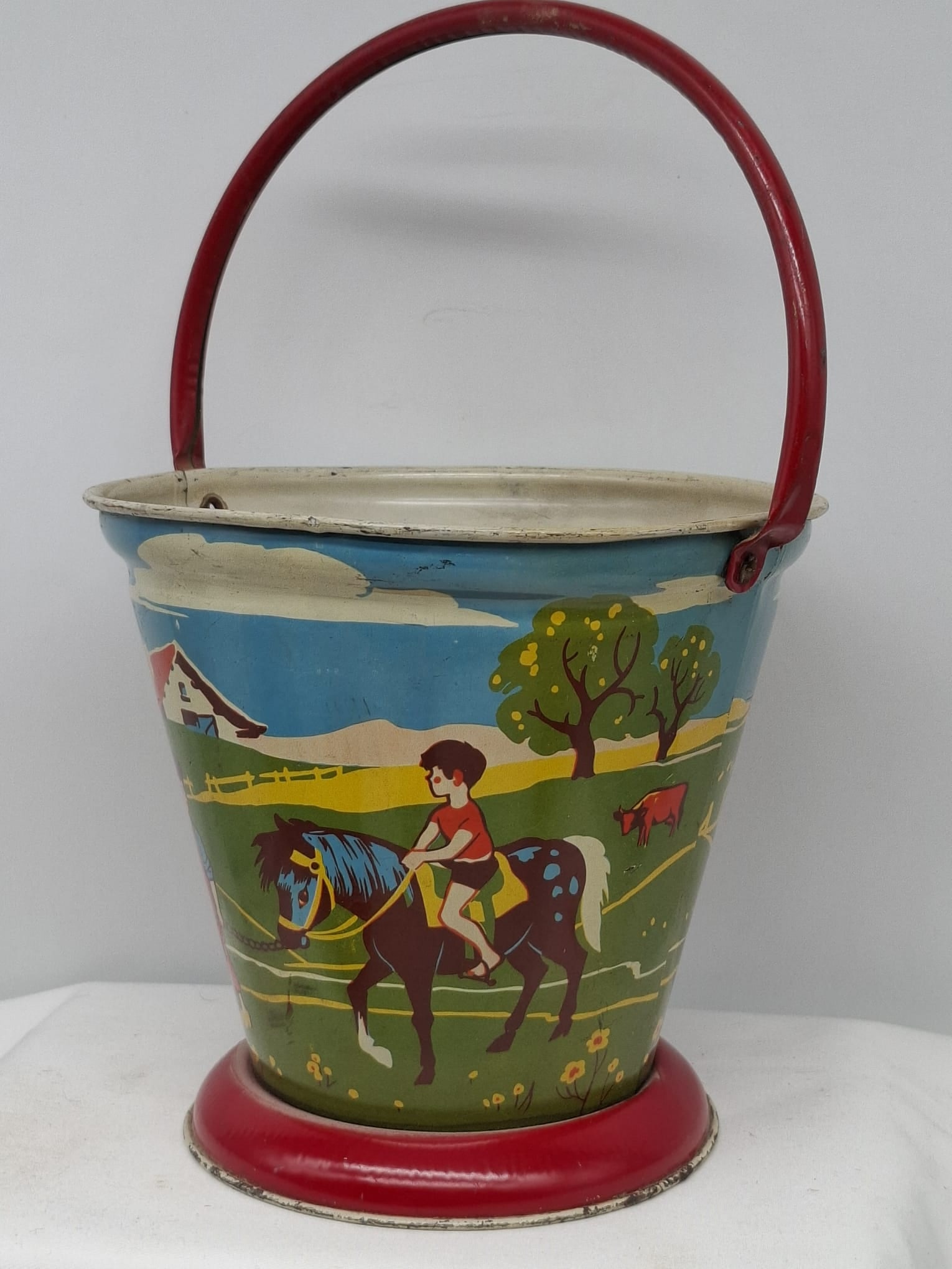 Early 20th Century Lithographed Tin Sand Pail – From Extensive European Collection: A charming and increasingly scarce early 20th century lithographed tin sand pail, exemplifying the colorful and imaginative design of classic seaside toys. This piece features vibrant period lithograp