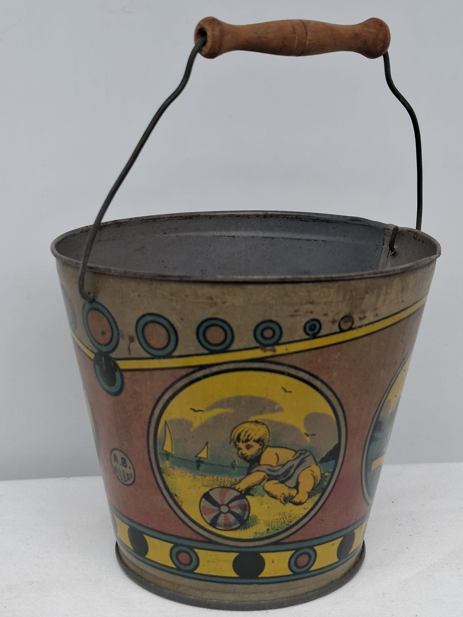 Early 20th Century Lithographed Tin Sand Pail – From Extensive European Collection: A charming and increasingly scarce early 20th century lithographed tin sand pail, exemplifying the colorful and imaginative design of classic seaside toys. This piece features vibrant period lithograp