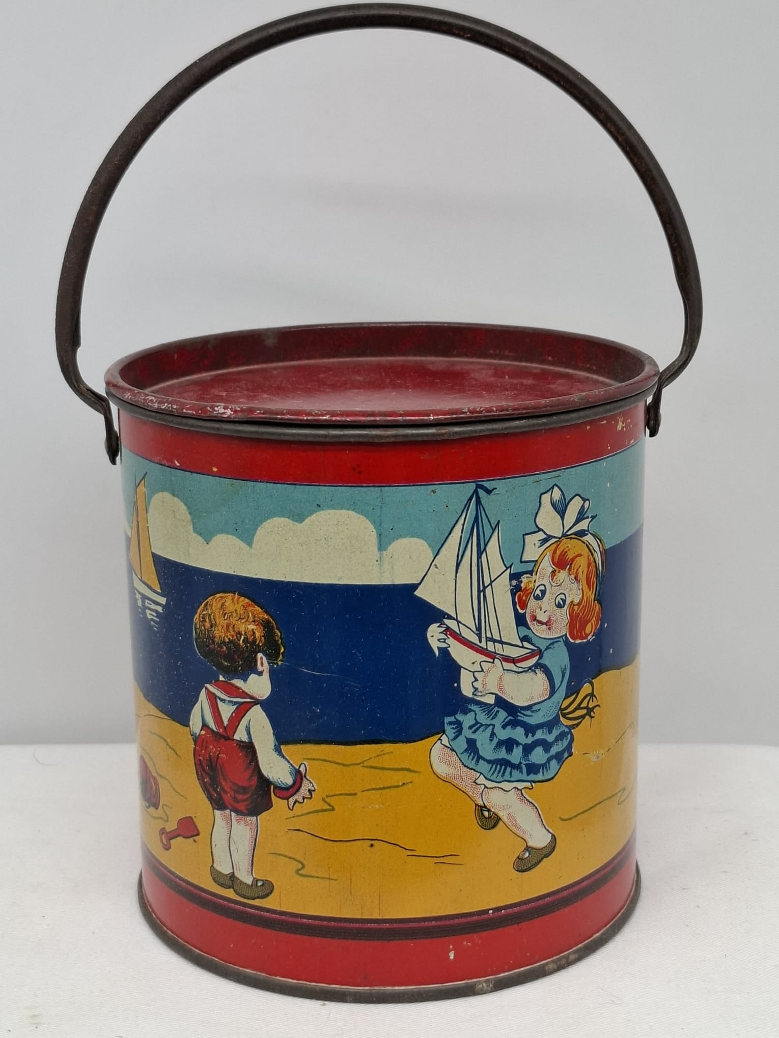 Early 20th Century Lithographed Tin Sand Pail – From Extensive European Collection: A charming and increasingly scarce early 20th century lithographed tin sand pail, exemplifying the colorful and imaginative design of classic seaside toys. This piece features vibrant period lithograp