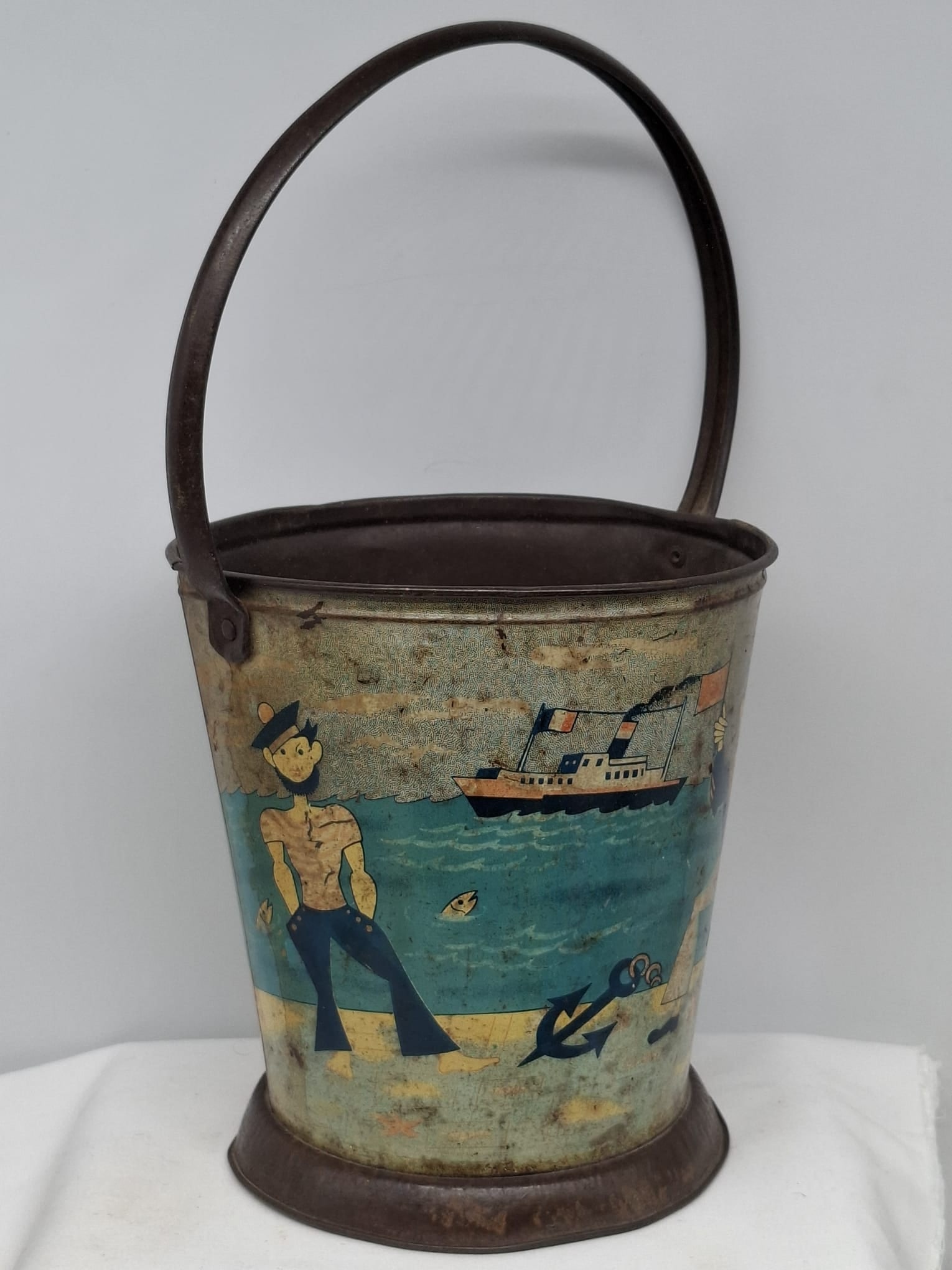 Early 20th Century Lithographed Tin Sand Pail – From Extensive European Collection: A charming and increasingly scarce early 20th century lithographed tin sand pail, exemplifying the colorful and imaginative design of classic seaside toys. This piece features vibrant period lithograp