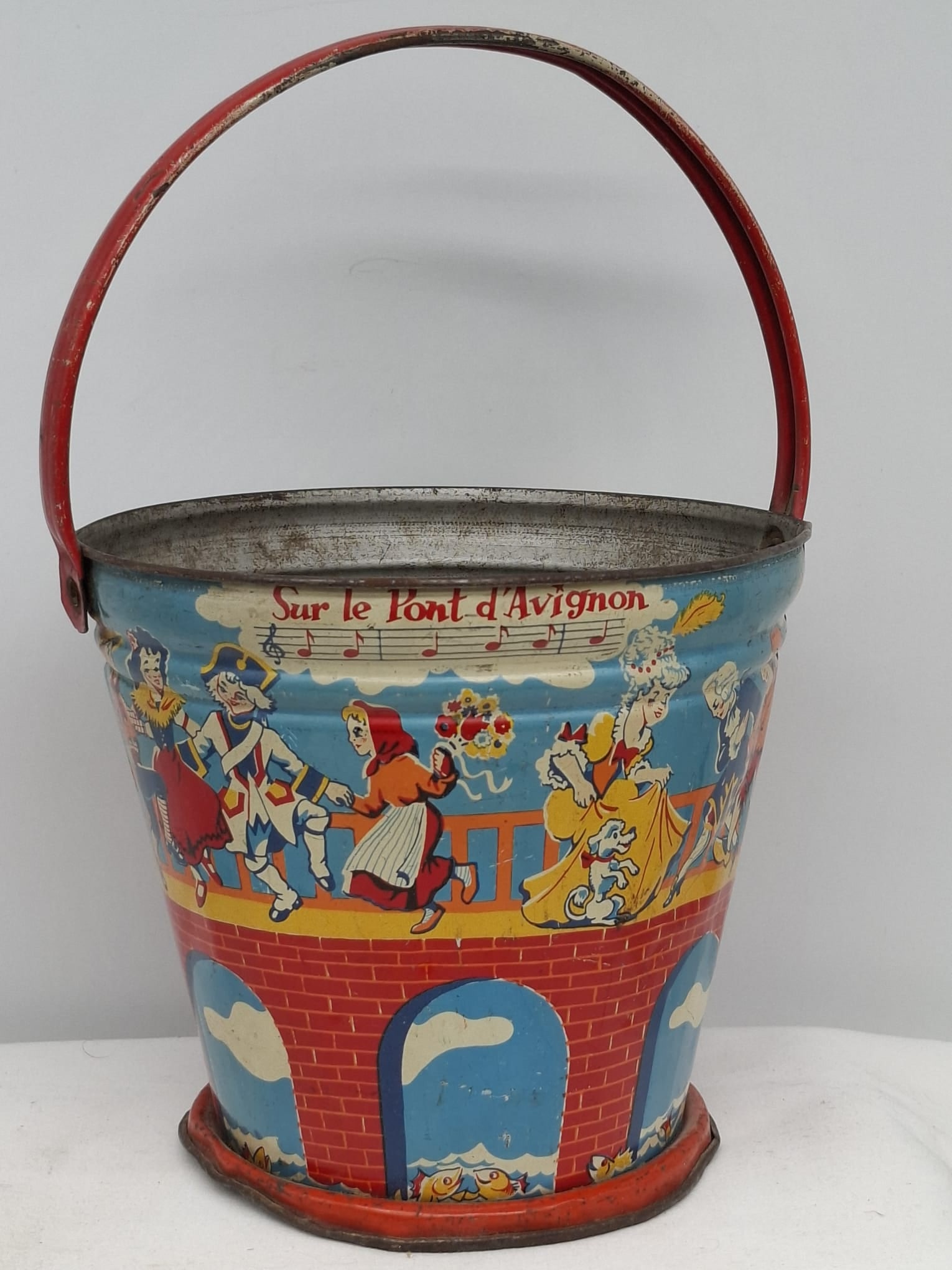 Early 20th Century Lithographed Tin Sand Pail – From Extensive European Collection: A charming and increasingly scarce early 20th century lithographed tin sand pail, exemplifying the colorful and imaginative design of classic seaside toys. This piece features vibrant period lithograp