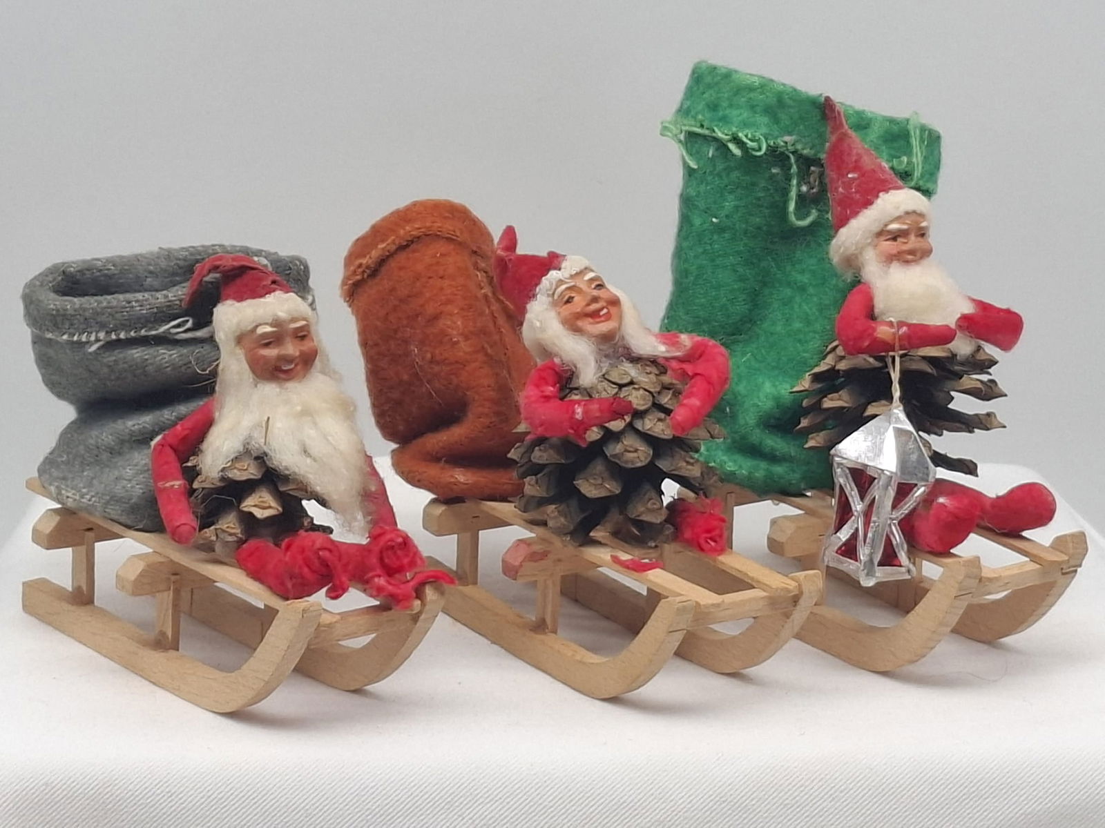 3 Pinecone Santa Candy Containers ~ Germany: Three nice antique/vintage Germany Santa Claus in sleigh candy containers, wooden sleigh with different color felt bags, paper mache faces, they are about 4 inches long, spun cotton arms and legs