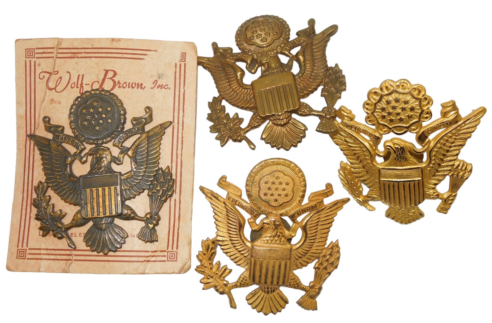 Lot (4) WWII US Army Officer Visor Cap Badges Amcraft Wolf-Brown: WWII US Army Officer Visor Cap Badges. Lot of (4). One piece is marked Amcraft and another is on its original Wolf-Brown card. Overall, good condition for their age.