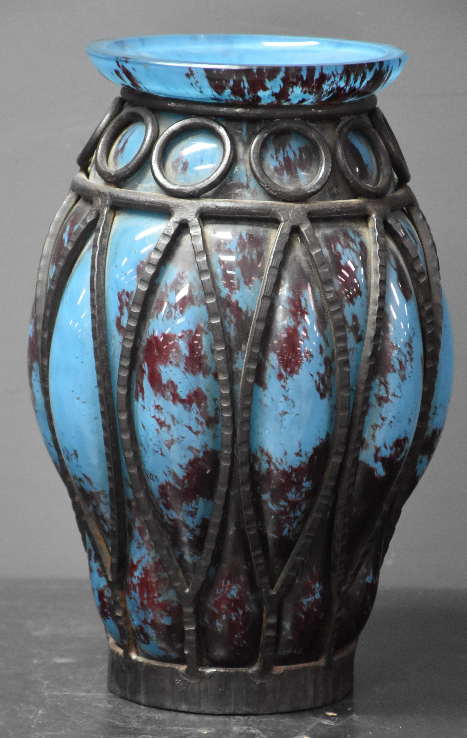 Art deco bluish glass vase in its wrought iron. French: Art deco bluish glass vase in its wrought iron. French work around 1930. In the style of Schneider or Daum Majorelle. Chip on the rim. Ht 25.5 cm.