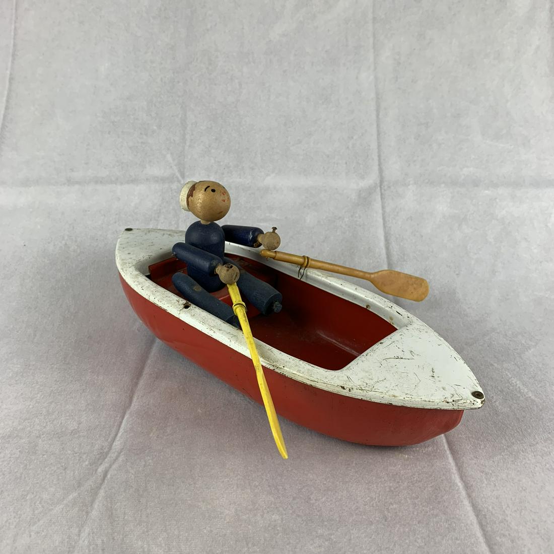 Vintage Wyandotte Metal Row Boat with Sailor: An interesting Wyandotte metal row boat with wooden sailor. Wheels on the bottom so that when rolled the sailor rows the boat. 12” long. Great condition with wear from use.