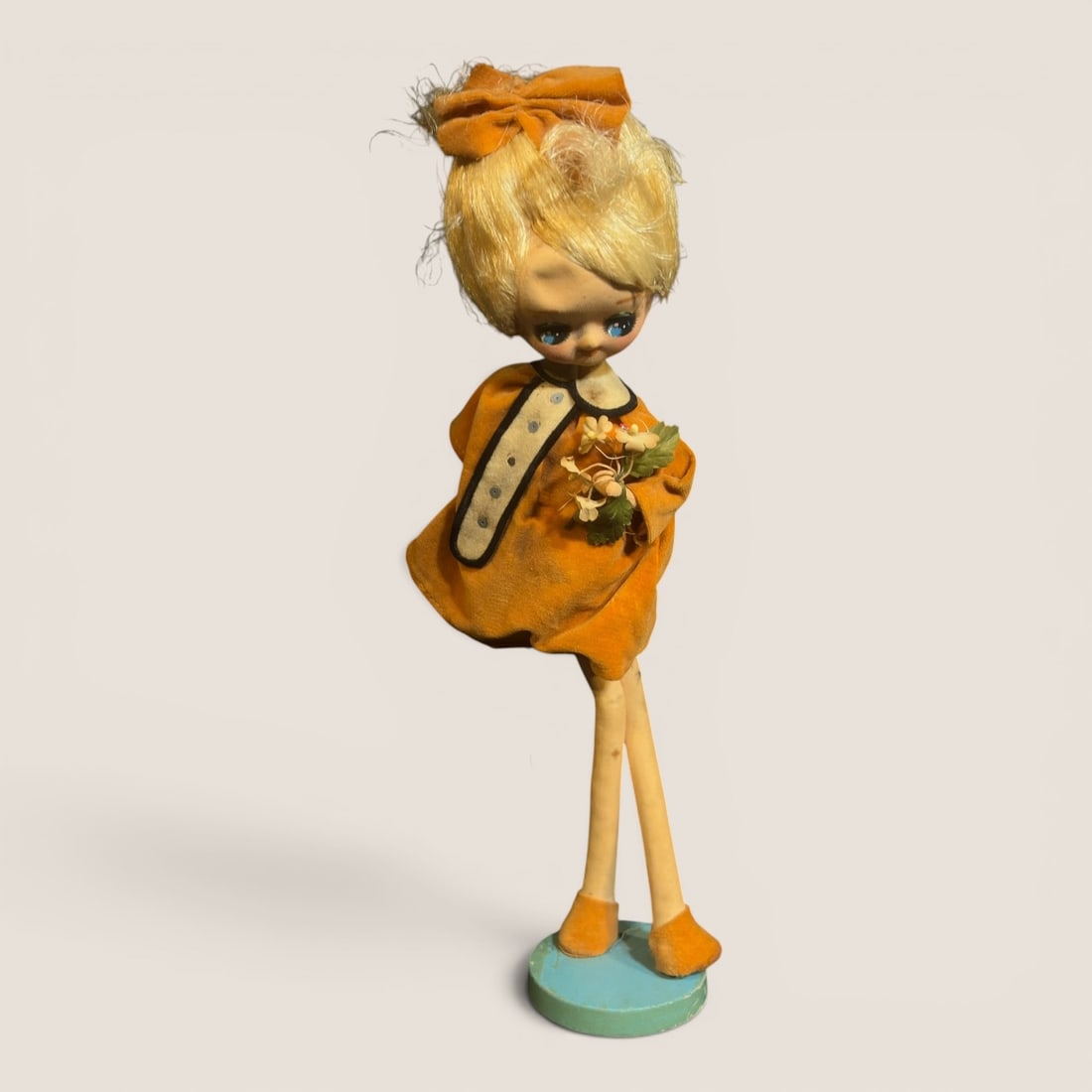 Vintage Big-Eyed Pose Doll in Orange Dress: This vintage posable fashion doll is designed in the style of big-eyed pose dolls popular in the 1960s and 1970s, resembling the work of companies like Bradley or Holiday Fair. The figure features a v