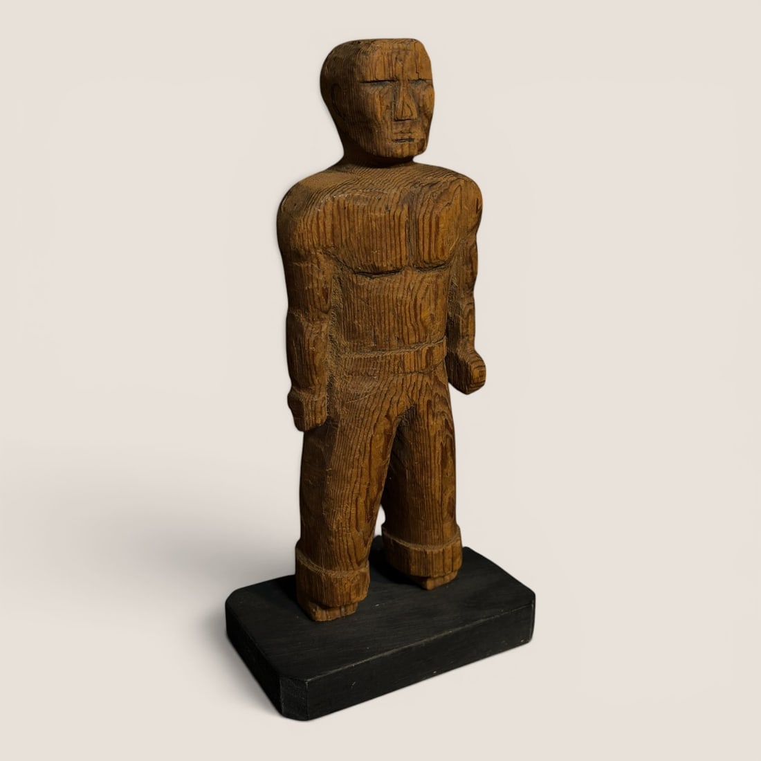 Rustic Carved Wood Male Figure on Plinth: This carved wood sculpture depicts a stylized male figure in a rustic folk art style. The piece is constructed from a block of softwood exhibiting prominent vertical tool marks and a natural grain pat