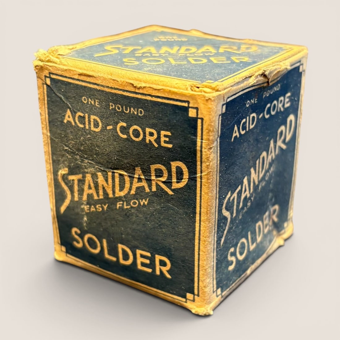 Vintage Standard Easy-Flow One Pound Acid-Core Solder Box: A mid-20th-century vintage cardboard box for Standard brand acid-core solder. The packaging is constructed from printed cardboard and features a dark blue background with yellow and gold-toned graphic