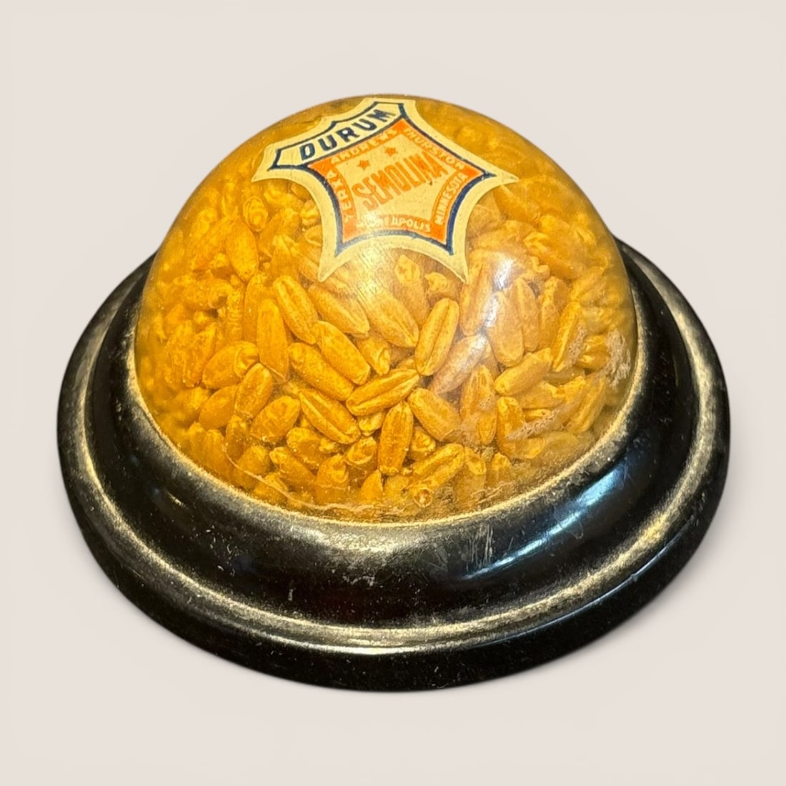 Andrews Thurston Durum Semolina Advertising Grain Paperweight: This vintage advertising paperweight and counter display was produced for the Andrews Thurston milling company based in Minneapolis, Minnesota. The object features a clear hemispherical dome, likely