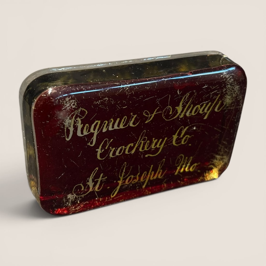 Antique Ruby Flash Glass Advertising Paperweight for Regnier & Shoup Crockery Co., St. Joseph,: This antique advertising glass paperweight features a rectangular form with rounded corners, constructed from a thick block of clear glass. The top surface is finished with a ruby-red flash or stain c