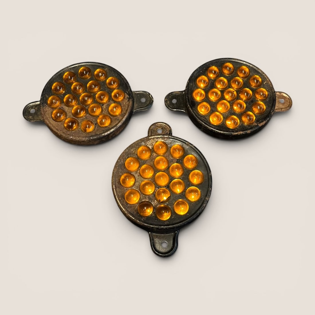 A Set of Three Vintage Amber Cat Eye Reflectors: This set of three vintage automotive reflectors, often referred to as cat eye or marble reflectors, features amber glass inserts. Each unit is constructed with a circular housing made from stamped ste