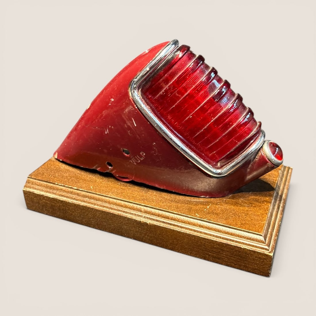 Vintage Automotive Rear Tail Light Assembly: A vintage automotive rear tail light mounted on a wood base, year and model unknown