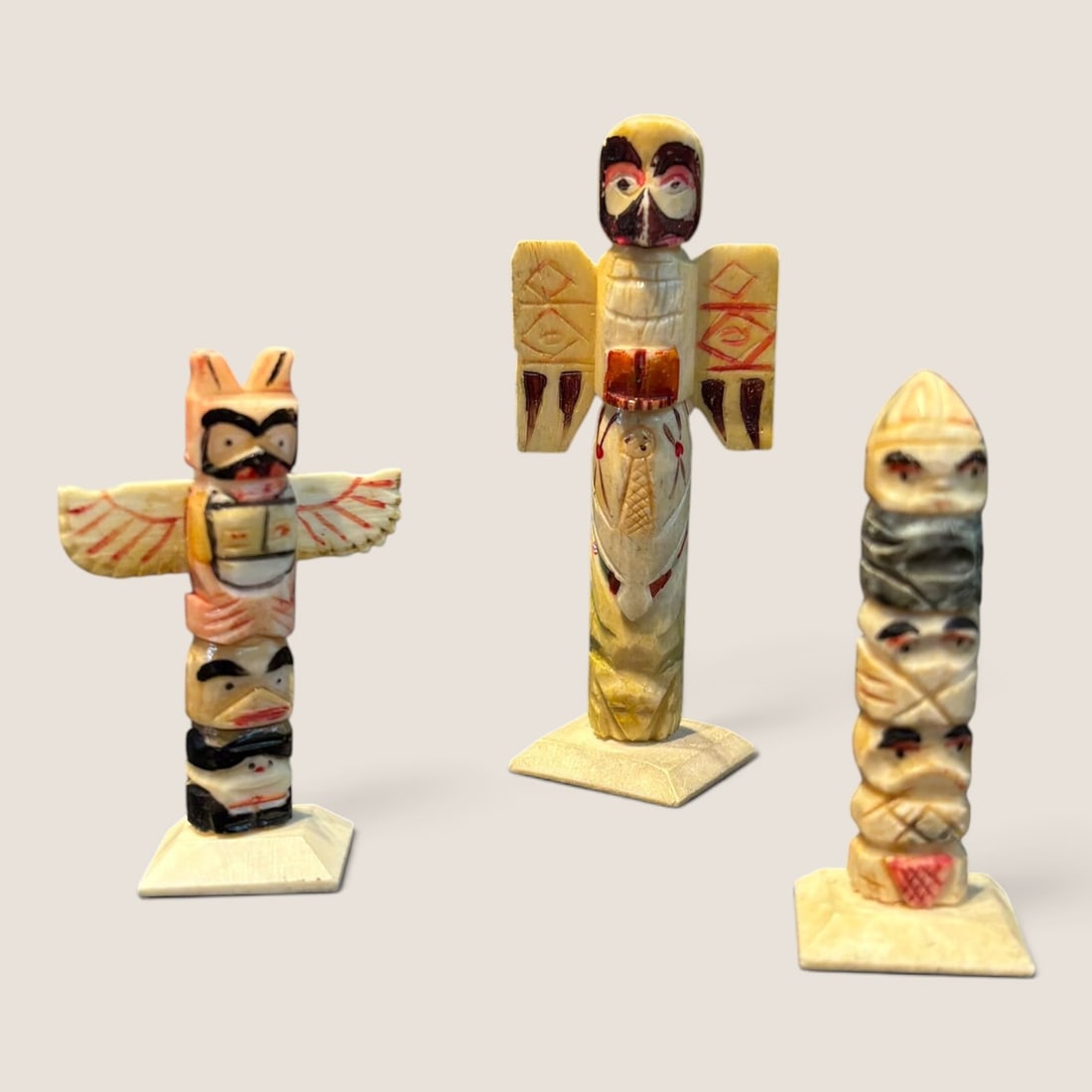 A Trio of Northwest Coast Carved Bone Miniature Totem Poles: A trio of miniature totem poles carved from bone, featuring traditional Northwest Coast Indigenous motifs and iconography. The sculptures represent stylized zoomorphic and anthropomorphic figures incl