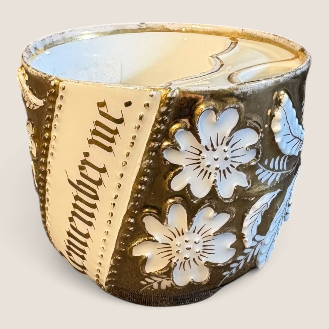Victorian Gilt Porcelain Mustache Cup with Remember Me Sentiment: A German porcelain mustache cup featuring a horizontal bridge across the interior rim designed to protect facial hair while drinking. The exterior is decorated with a diagonal cream band bearing the p