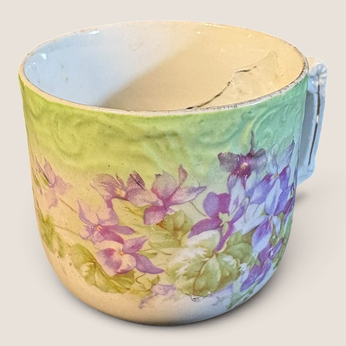 Late Victorian Relief Molded Porcelain Cup with Violet Decoration: An antique porcelain cup featuring a relief-molded scroll pattern on the upper portion of the body. The exterior surface is decorated with a lime green and cream gradient ground, over which are transf