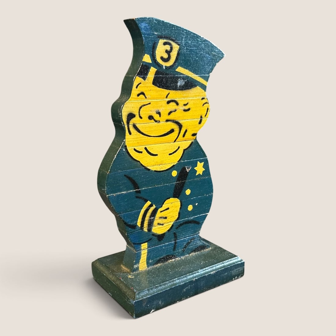 Mid-Twentieth Century Painted Wood Policeman Figural Cutout: A mid-twentieth-century painted wood figural cutout depicting a stylized, smiling policeman. The character is shown in a three-quarter profile and is mounted to a matching rectangular wooden base. The