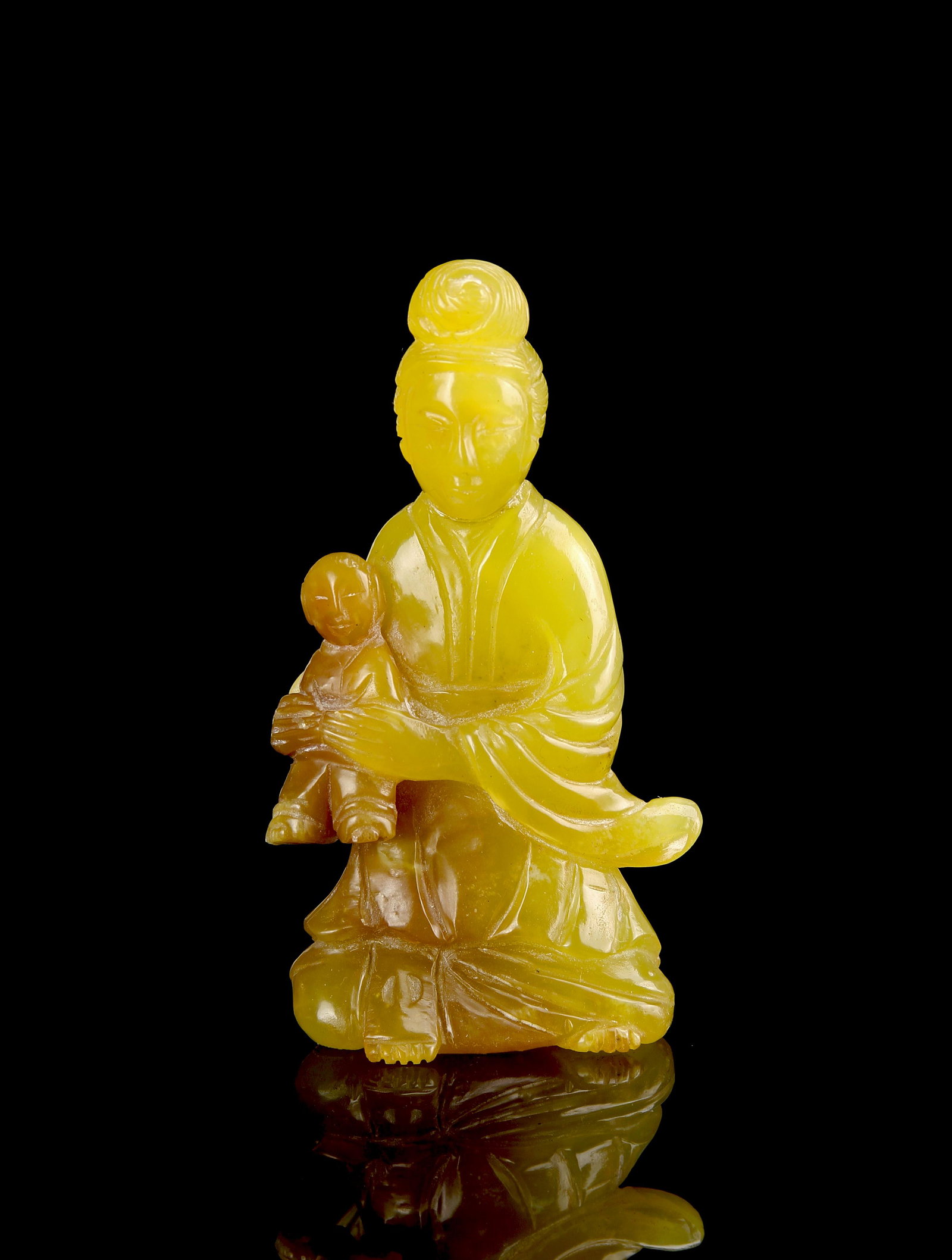 Chinese Yellow Jade Guanyin: China, 19th Century, yellow jade Guanyin, intricate carving with flat base, seated wearing flowing robes and holding a small child, with deep yellow natural shading throughout. Height 3 1/2 in.