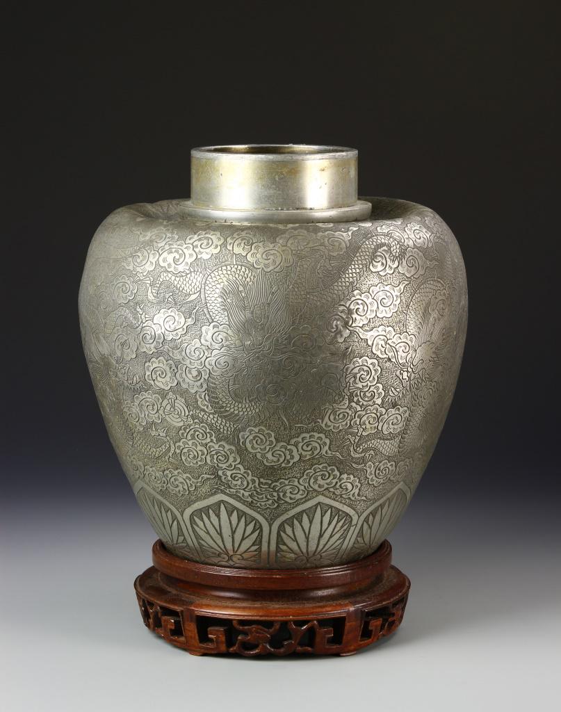Chinese Metal Jar: China, 19th C., metal jar with base, dents, wide mouth with plain, thick neck, wide shoulders, tapering sides to flat base, placed on carved wooden stand, incised floral decoration. Height 11 1/2 in.