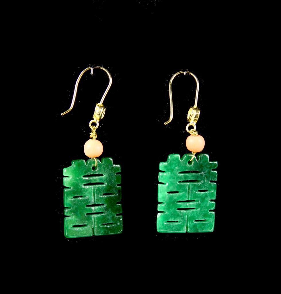 Pair of Chinese Jadeite Earrings: China, pair of jadeite earrings, oblong shaped with carved open details in geometric design, topped with a small coral bead in pale pink with gold threads. Height 1 in.
