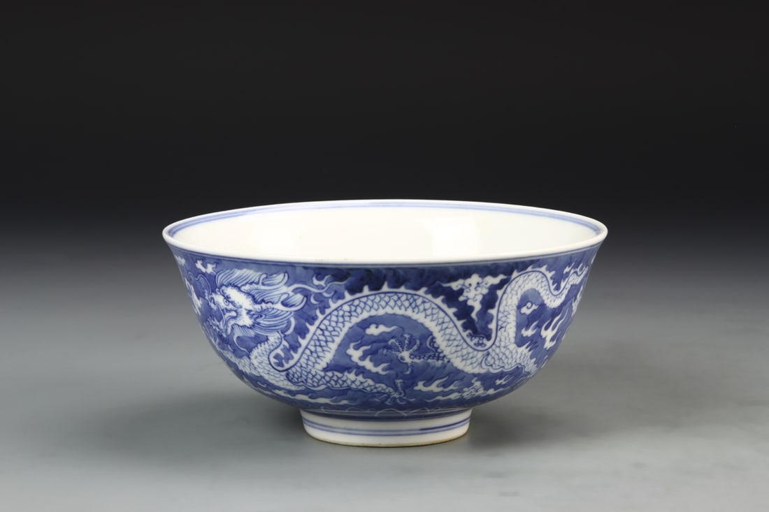Chinese Blue and White Dragon Bowl: China, Qing Dynasty, blue and white bowl, deep potted dish, flared mouth, high sides tapering to high footed base, decorated with a dragon amid clouds and curled dragon in the center, Kangxi mark. Wid
