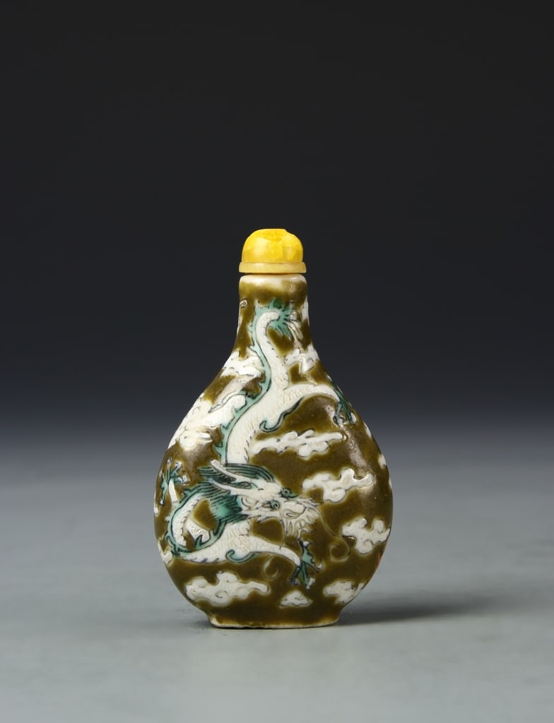 Chinese Famille Rose Snuff Bottle: China, Qing Dynasty, famille rose snuff, ovoid body taper into neck, with a delicately incised yellow stopper, dragon and cloud motif on a brown ground. Height 2 1/2 in.