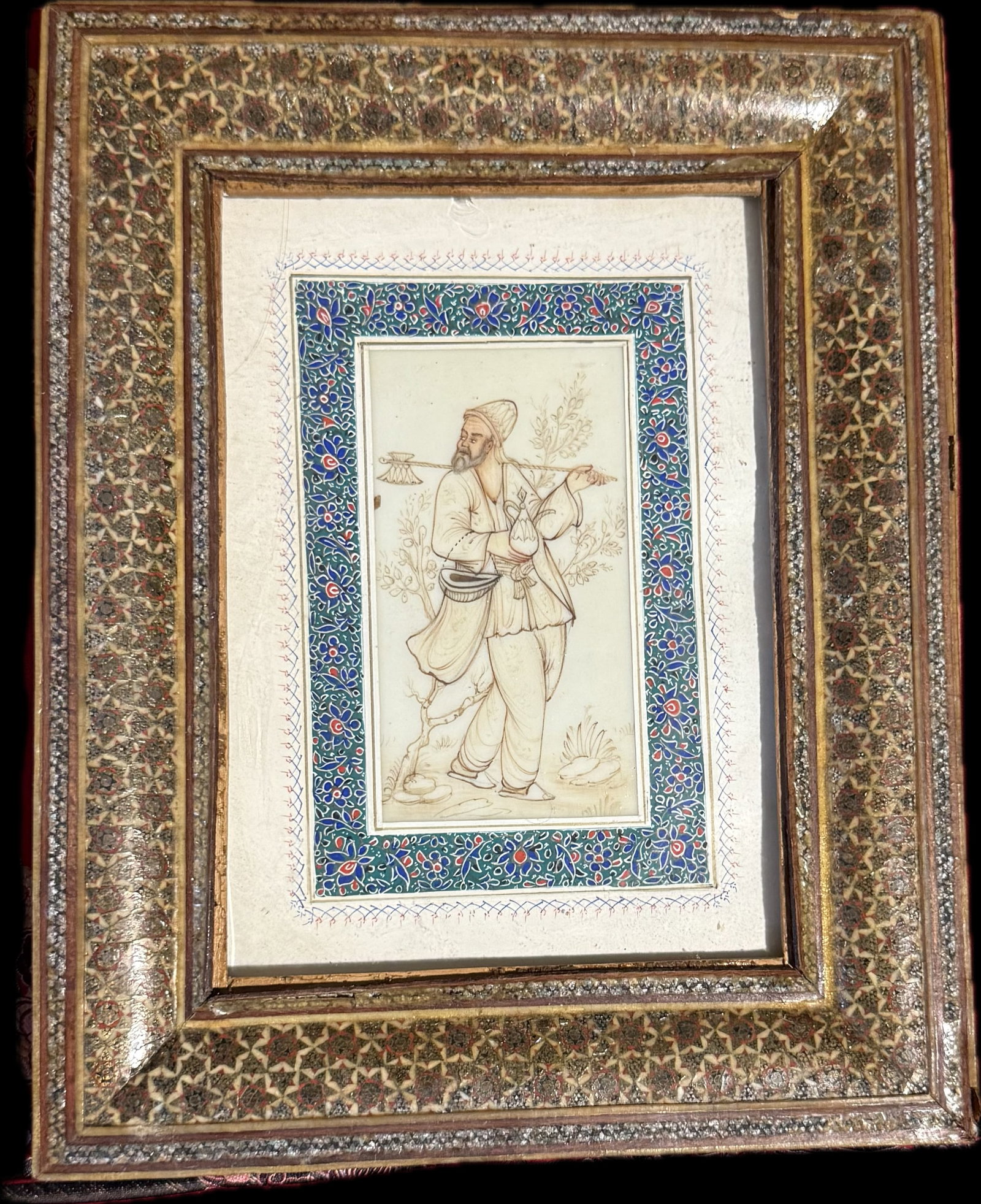 A framed Persian miniature painting: A framed Persian miniature painting, likely featuring a figure in traditional attire within a decorative border. The frame itself appears to be crafted using Khatam Kari, a traditional Persian marquet