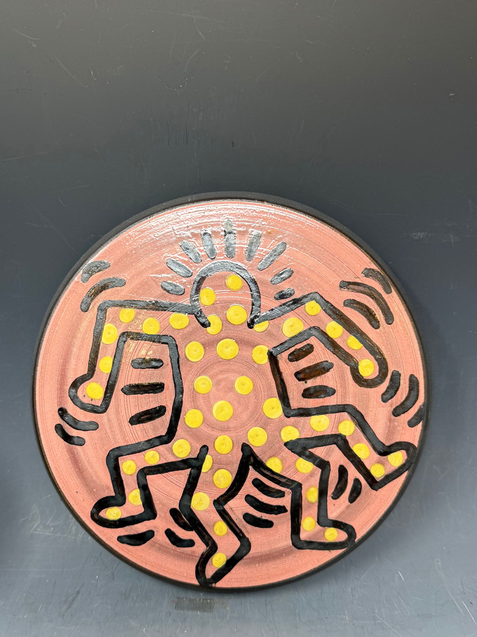 A porcelain plate featuring a dancing figure with a signature of P. Harings 87: A porcelain plate featuring a dancing figures in yellow and black on a pinkish with a signature of P. Harings, 87, 8” D