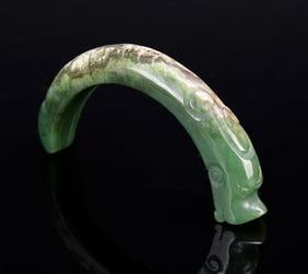 Antique Chinese Jade Dragon: China, antique Jade Dragon, in a semi-circular form, with geometric carved detail along the body, in a mottled green and brown hue with striations on the stone. Length 4 in.