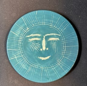 A light blue round pottery hanging round plaque with Picasso print on the back: A light blue round pottery hanging round plaque with stylized human face and printed name of Picasso on the back, 8 1/2” D