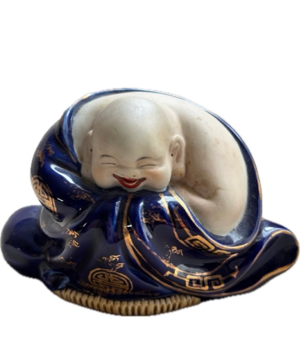 A Chinese Porcelain Laughing Buddha (Budai) figurine: A Chinese Porcelain Laughing Buddha (Budai) figurine, often stylized with a reclining pose and detailed robes. Subject: Representing the monk Budai, known as a symbol of happiness, abundance, and good