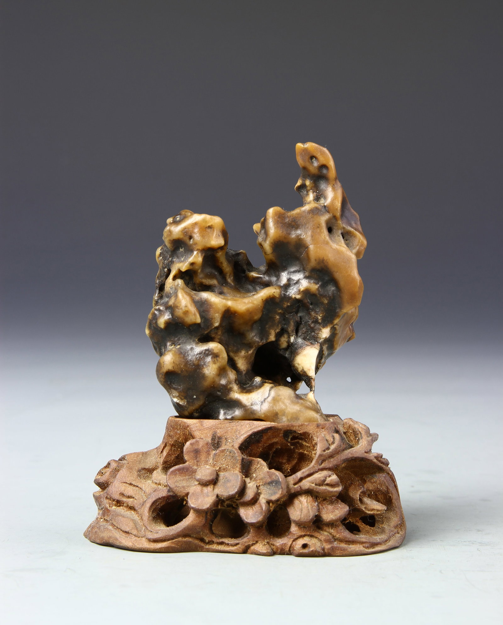 Chinese Scholar on Base: China, 19th C., scholar on base, organic in form, base has a floral motif, varying hues of brown. Height 3 in.