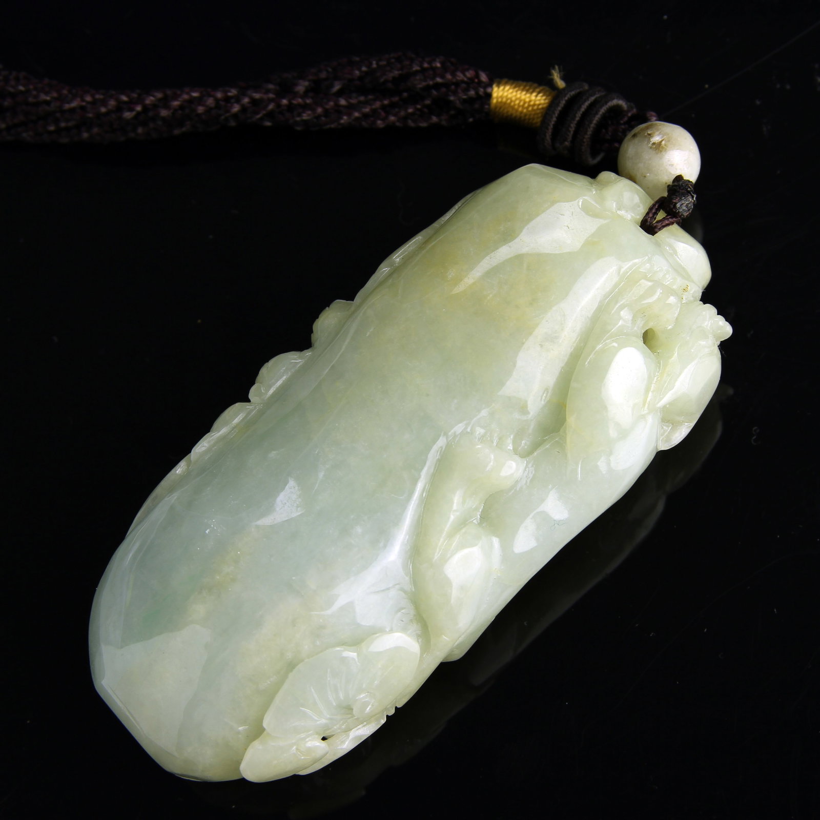 Chinese Jadeite Ornament: China, well-carved jadeite ornament, in an elongated form, with natural elements, and a mythical creature clinging to the side, pierced for hanging. Length 3 3/4 in.