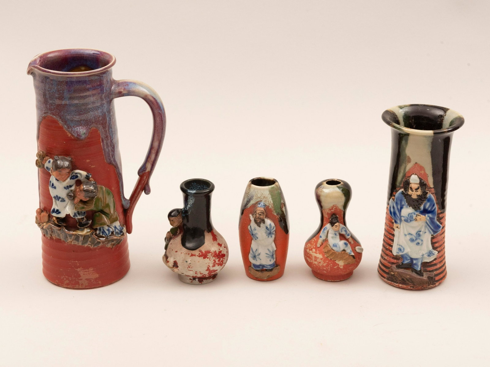 Five Pieces of Japanese Sumida Gawa Art Pottery Height: Five Pieces of Japanese Sumida Gawa Art Pottery Each with applied figures the largest pitcher with an amusing scene of children playing; together with four vases. Height of tallest: 8 1/4 inches