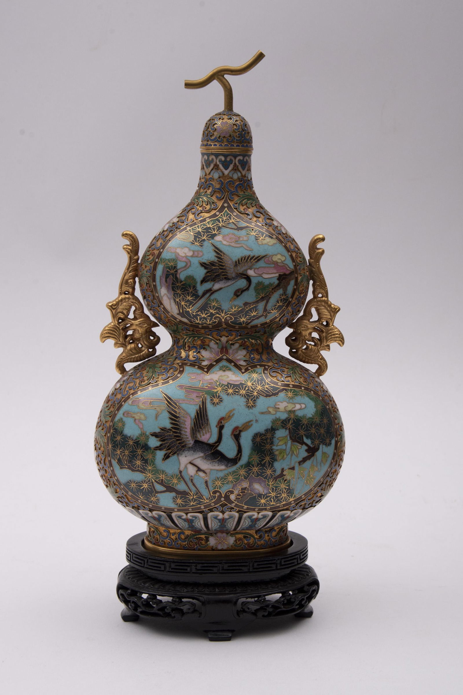 Cloisonné Enameled Lidded Gourd Shaped Vase 11" tall: Cloisonné Enameled Lidded Gourd Shaped VaseThe 2 handled vase gilt with phoenix style handles and central medallions of birds within a tree lined scene.On a carved wood stand11" tall exclusive o