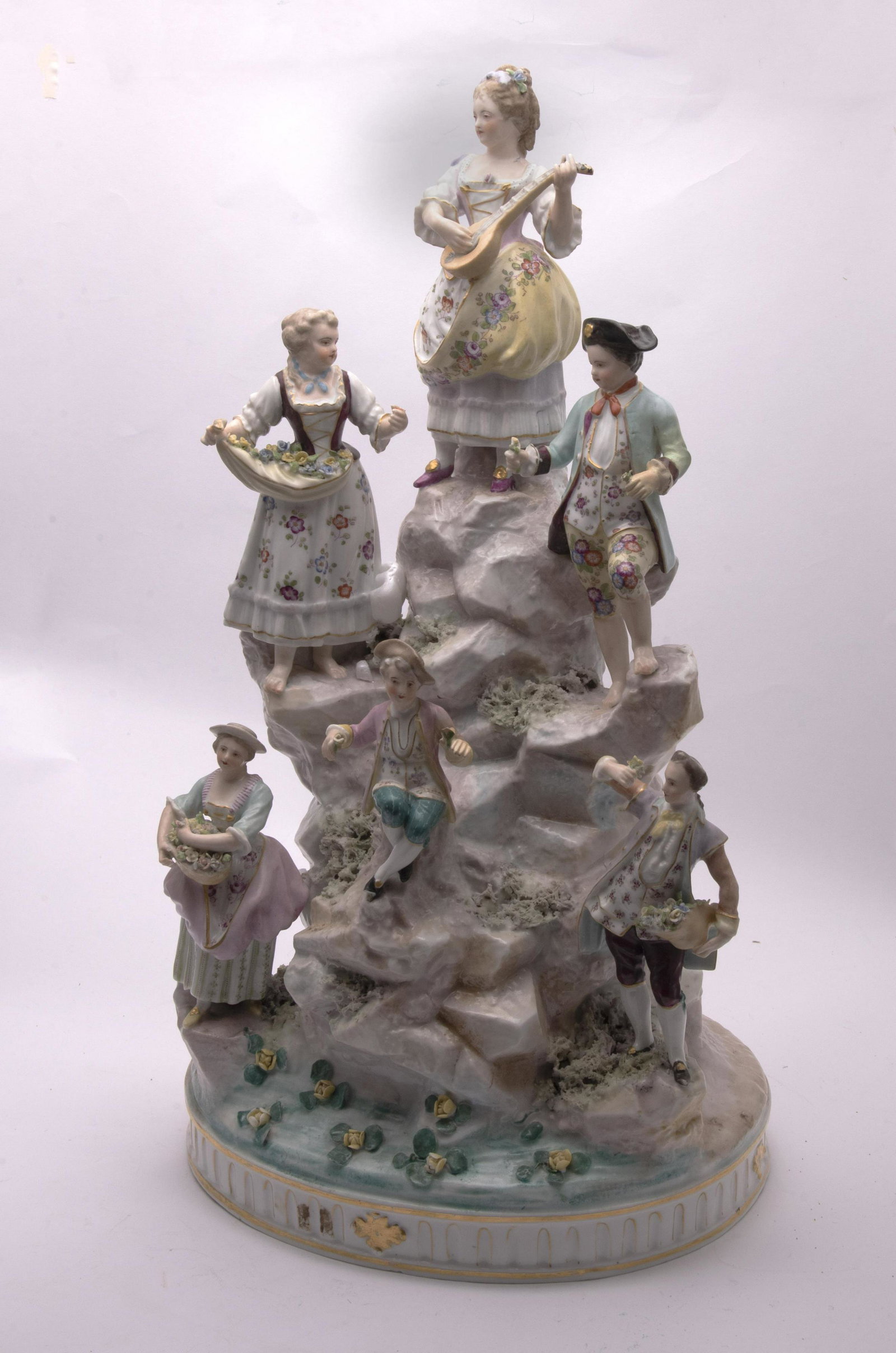 19th Century Meissen Style Porcelain Centerpiece 21.5": 19th Century Meissen Style Porcelain Centerpiece Large 6 figure grouping depicting multiple figures on a rocky mountain base. Figures holding baskets and bundles of flora and the central figure playin