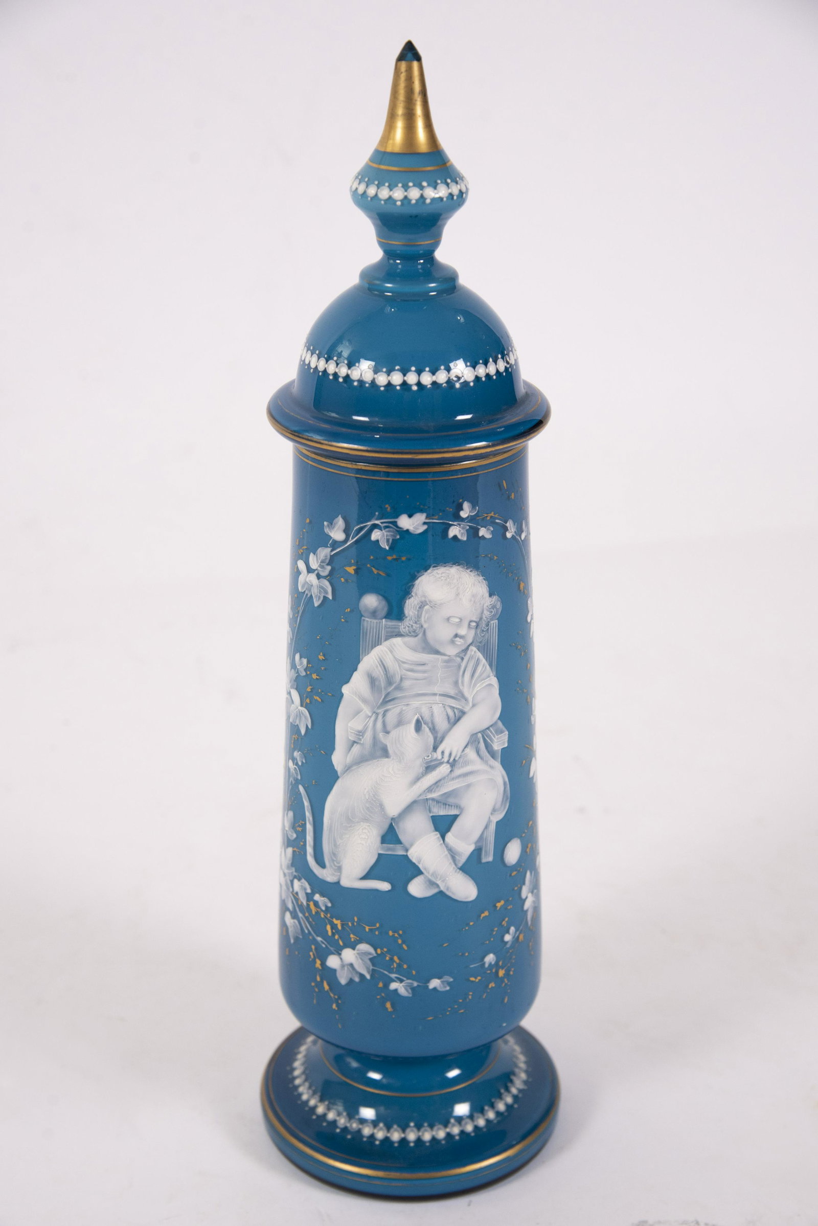 An Unusual Mary Gregory Style Glass Pokal: An Unusual Mary Gregory Style Glass Pokal The tall lidded vessel nicely enameled with a small sleeping child and a cat sneaking a treat. Attractive blue satin type glass with gilded highlights 18"