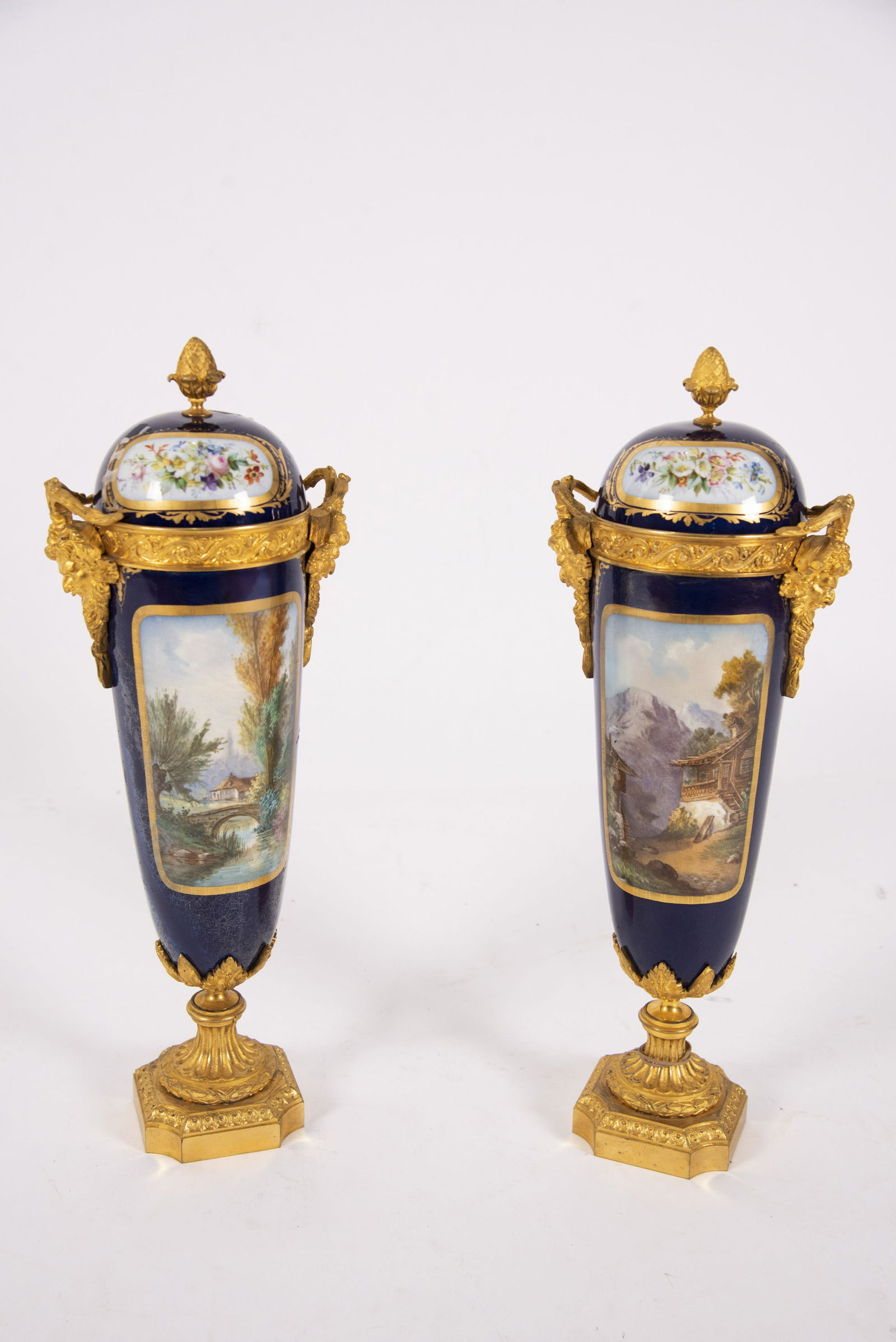 A Pair of Sevres Style Porcelain and Bronze Dore: A Pair of Sevres Style Porcelain and Bronze Dore Mounted UrnsEach urn with heavily gilt bronze mounts and satyr handles. Scenes depicting young couples in a country setting on the front and a village